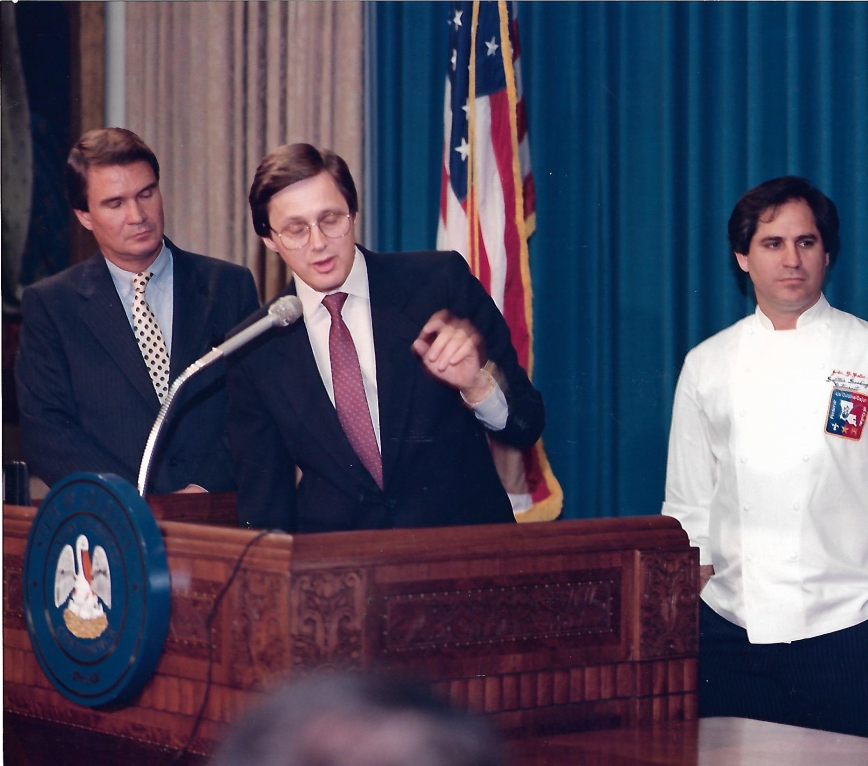 David N. Young speaking at a podium with U.S. Sen. John Breaux and Chef John D. Folse in Louisiana